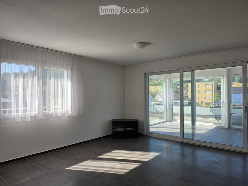Empty room with tiled floor, large sliding glass doors leading to a balcony, and sheer white curtains on the windows.