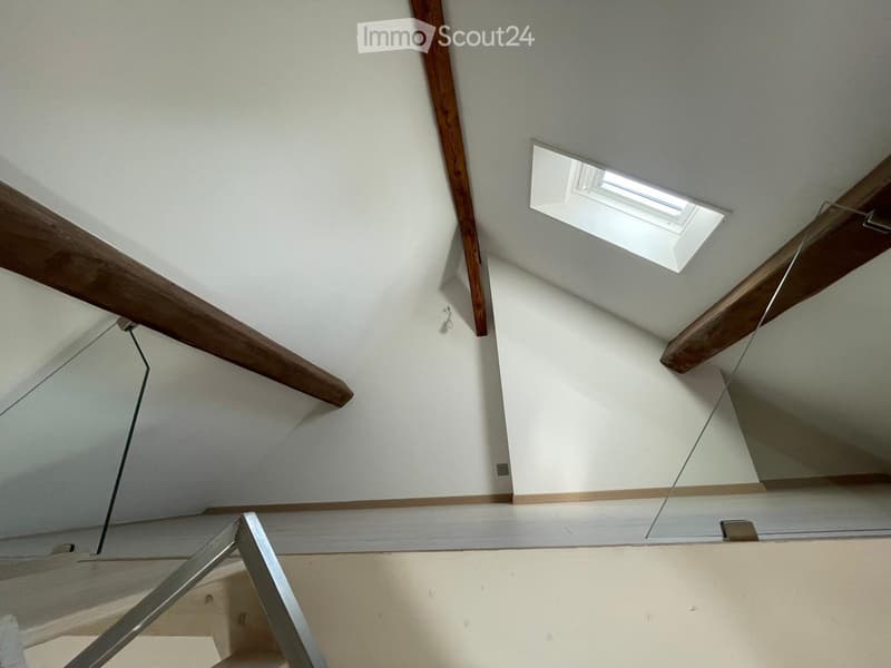 Empty hallway with exposed wooden beams, white walls, and a skylight window providing natural light.