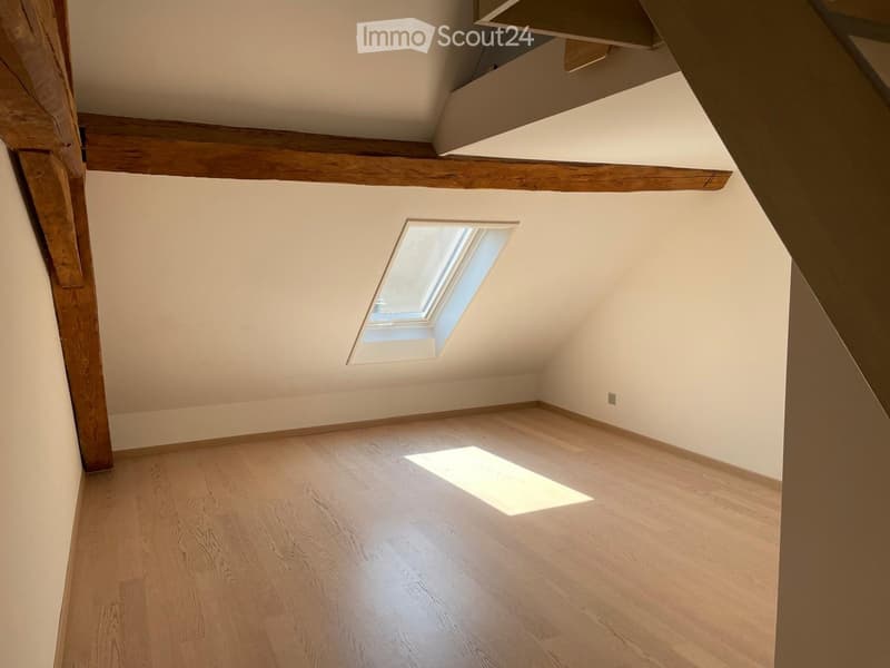 Empty attic room with wooden floor, exposed wooden beams, and a skylight window letting in natural light.