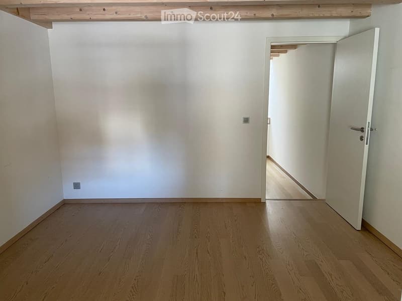 Empty room with light wooden flooring and white walls, featuring a partially open door leading to another space.