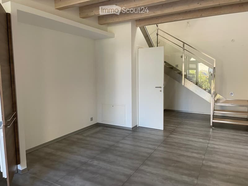 Empty hallway with tiled floor, white walls, and a staircase leading upwards with a glass railing.