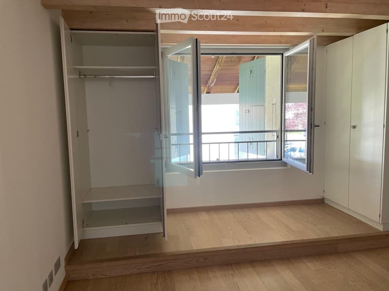 Empty room with wooden flooring, built-in closet with open shelves, and large window with balcony access.