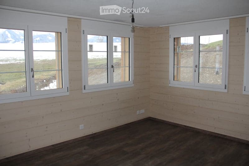 Empty room with wooden walls and flooring, large windows with white frames, and visible electrical outlets.