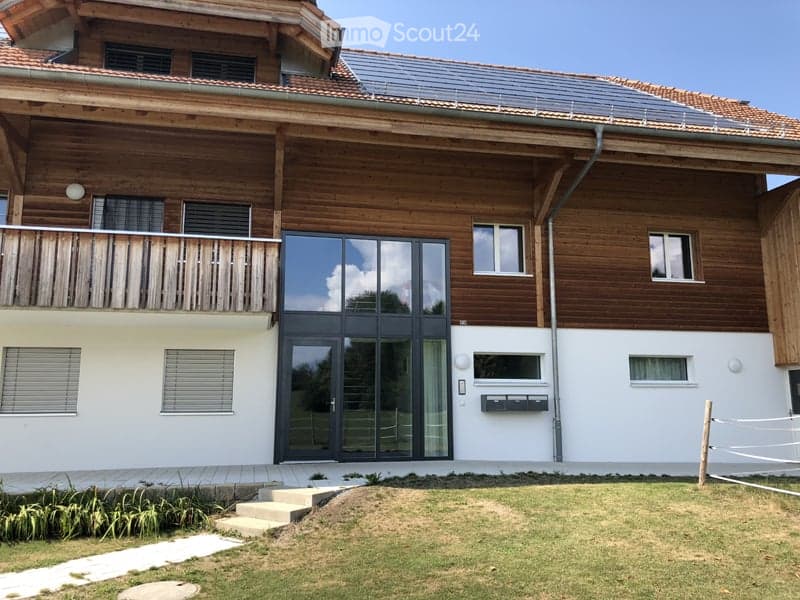 Modern two-story house with wooden facade, large balcony, and solar panels on the roof.
