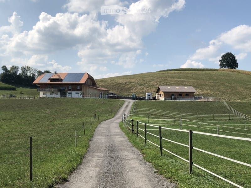 Rural farmstead with a large barn, smaller outbuilding, fenced pasture, and solar panels on the roof.