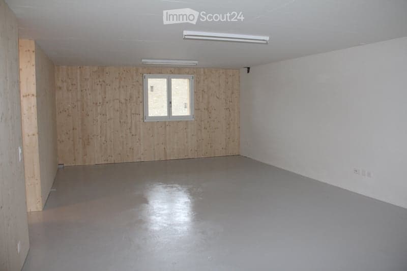 Empty room with wooden panel walls, grey concrete floor, and a single window with white frame. No furniture or equipment present.