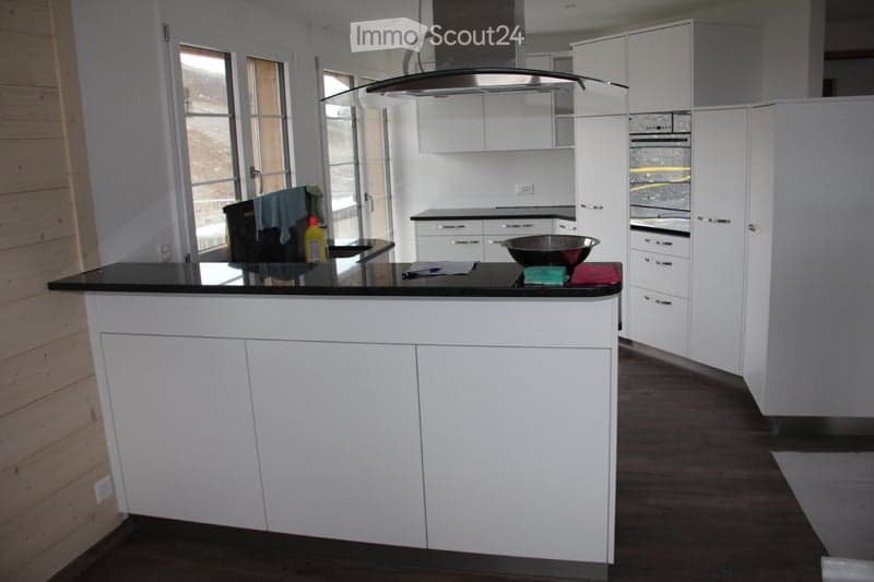 Modern kitchen with white cabinets, a central island, and stainless steel appliances. The island features a black countertop with a bowl and a bottle on it.
