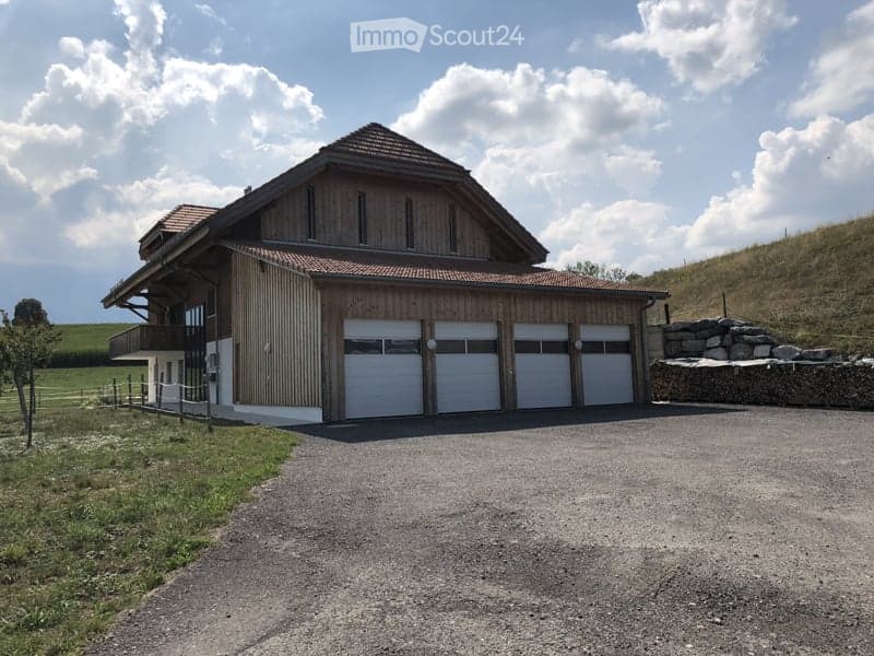 Modern two-story house with wooden exterior, large garage, and balcony on the upper level.