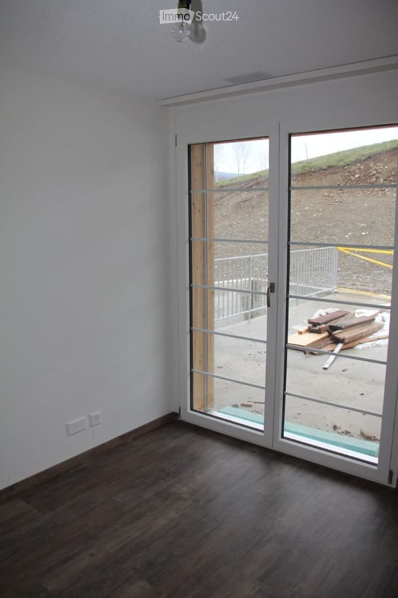 Empty room with dark wooden flooring, white walls, and large glass sliding doors leading to an outdoor area.
