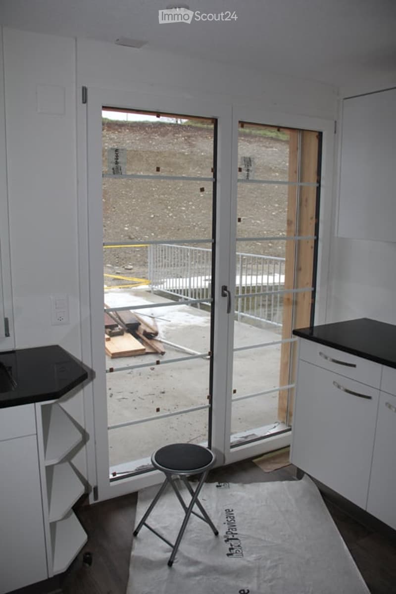 Empty room with white walls, dark countertops, a small black stool, and a large sliding glass door leading to an outdoor area.