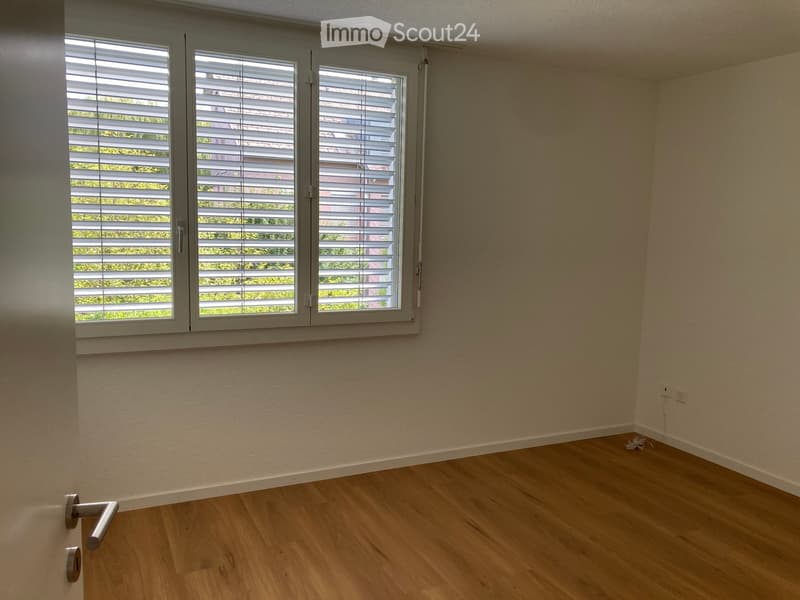 Empty room with light wooden flooring, white walls, and large window with blinds. No furniture or equipment present.