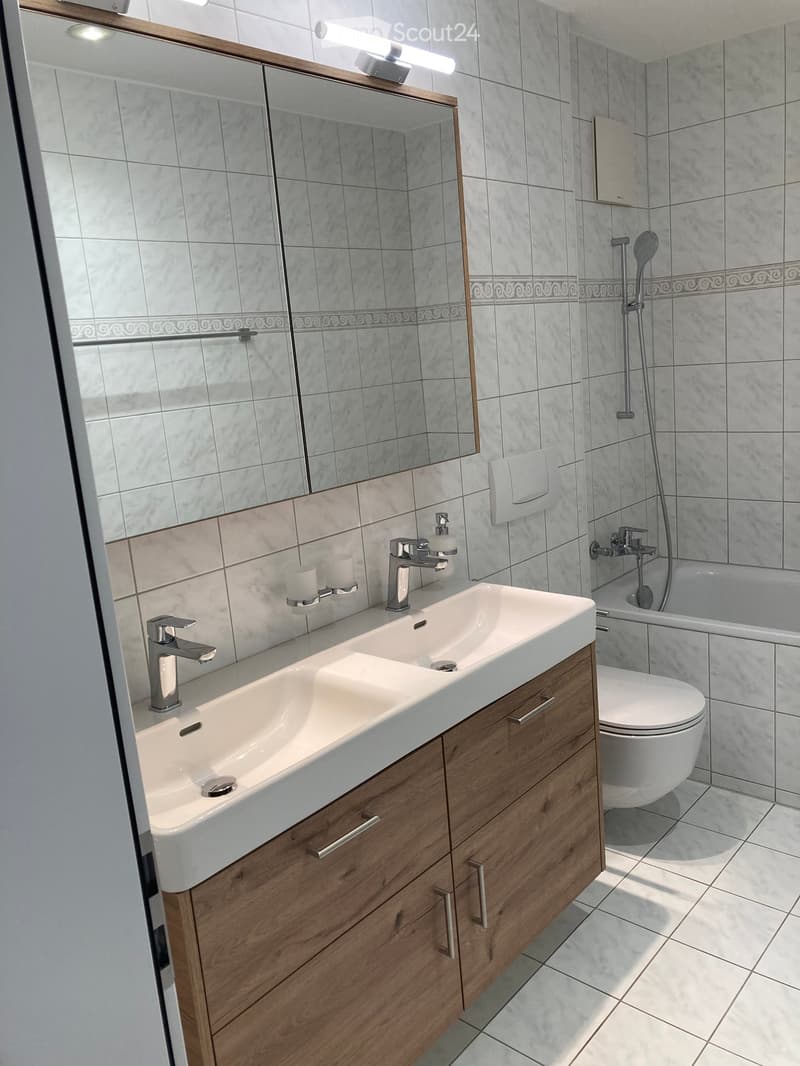 Modern bathroom with a double sink, wooden cabinet, mirror, toilet, and shower area.