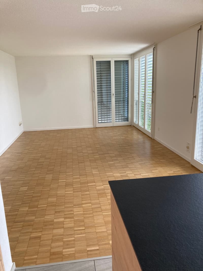 Empty room with wooden flooring, large windows with blinds, and white walls.