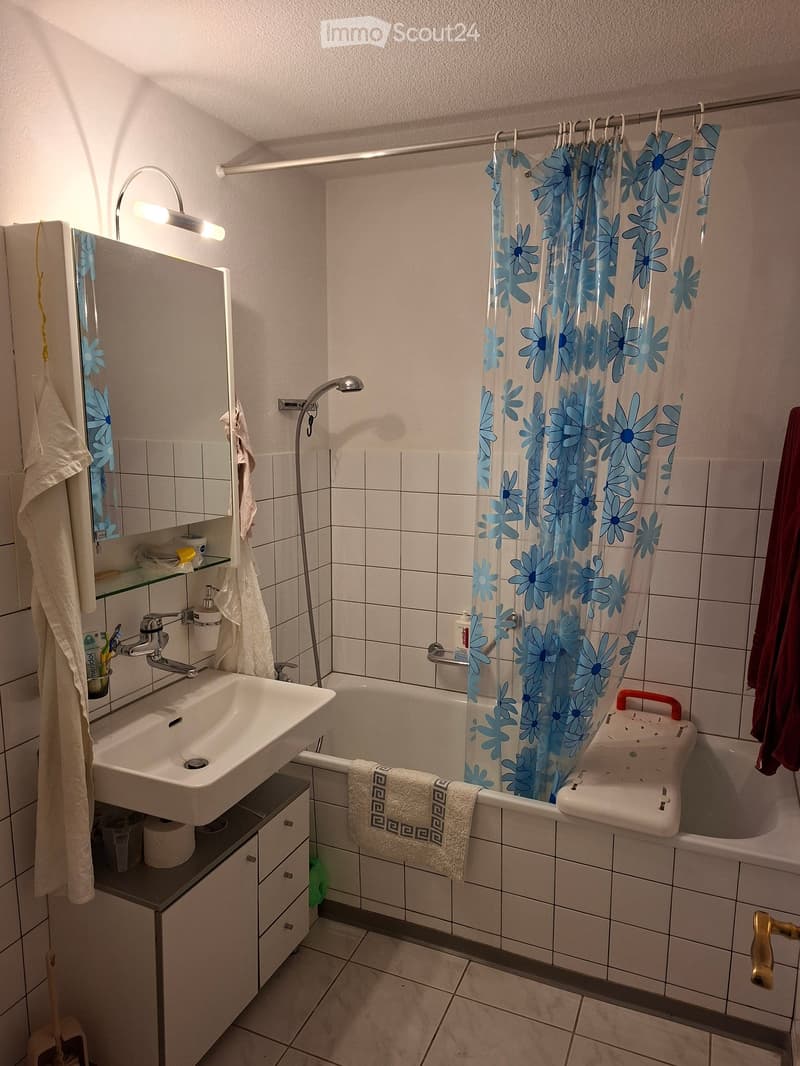 Bathroom with white tiles, a sink, a mirror, a bathtub with a blue floral shower curtain, and a towel on the edge of the tub.