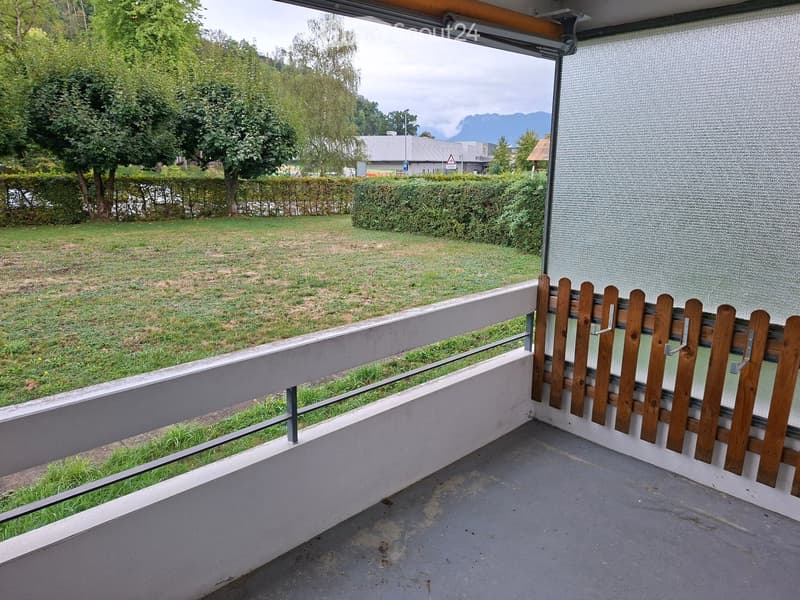 Balcony with wooden fence, metal railing, and view of a grassy area with trees and distant mountains.