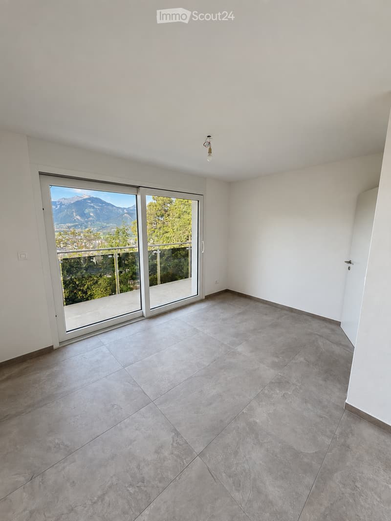 Empty room with large sliding glass doors leading to a balcony, offering a scenic mountain view. The room features light-colored tiled flooring and white walls.