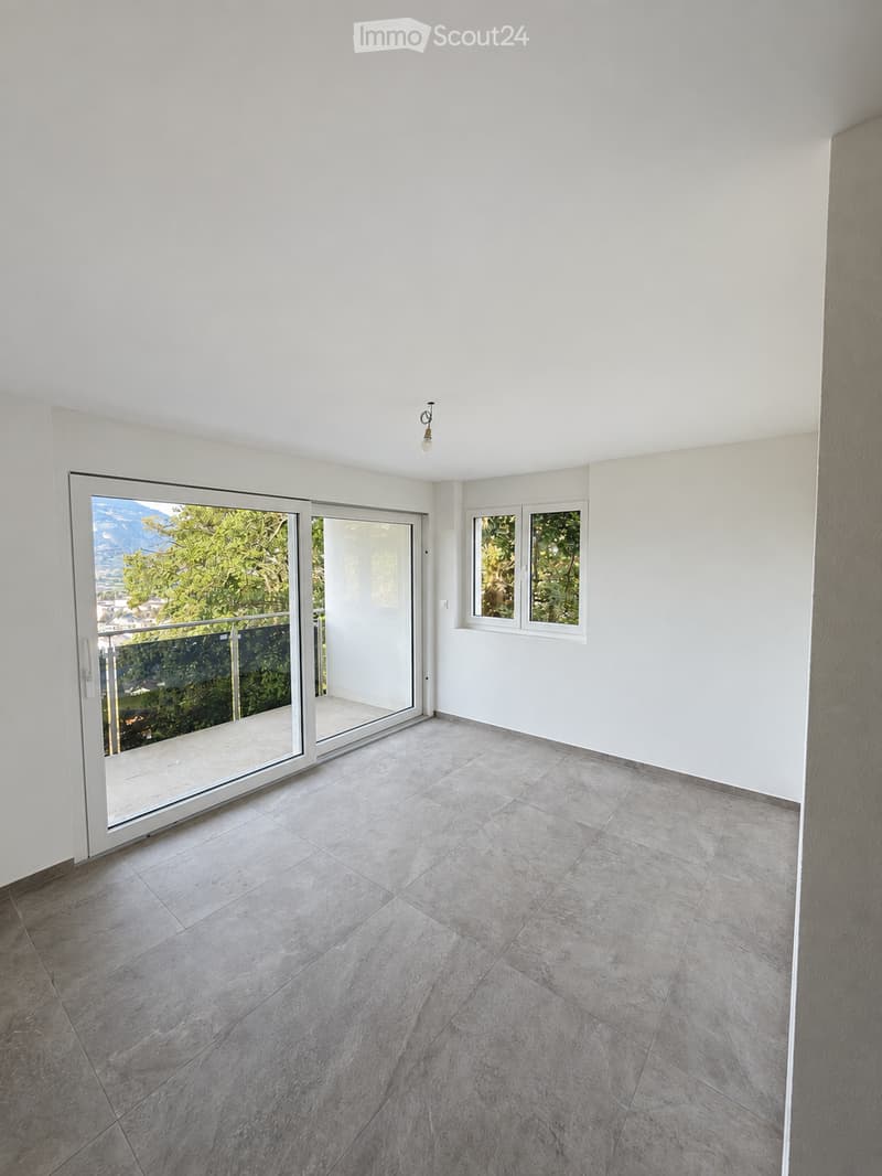 Empty room with large sliding glass doors leading to a balcony, tiled floor, white walls, and a view of greenery and mountains.