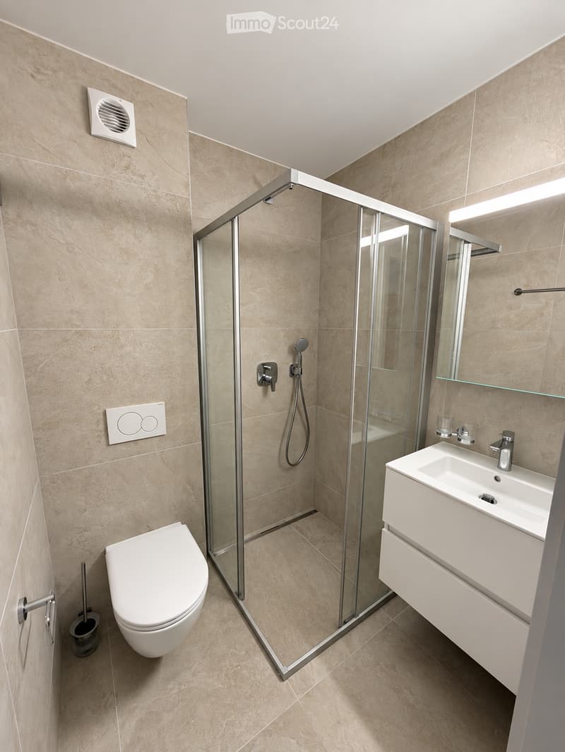 Modern bathroom with beige tiles, a glass-enclosed shower, a white toilet, a white sink with a modern faucet, and a built-in mirror cabinet.