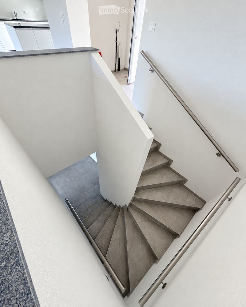 Modern staircase with gray tiled steps and metal railings, white walls, and a view into an adjacent room with a countertop and sink.