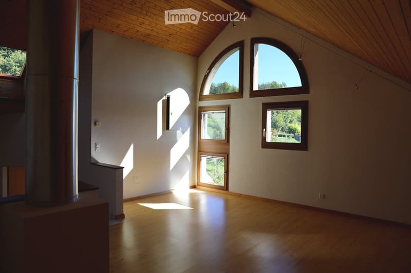Bright, empty room with wooden flooring and exposed wooden ceiling beams. Features large arched windows and a door leading outside, allowing natural light to fill the space.