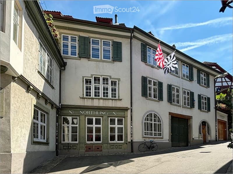 A two-story building with a light-colored facade, multiple windows with shutters, and a sign reading "NORTHILING" above the entrance. Two flags are displayed on the right side of the building.