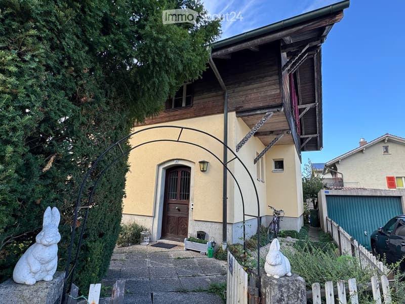 Two-story house with yellow facade, wooden balcony, and stone pathway leading to the entrance.