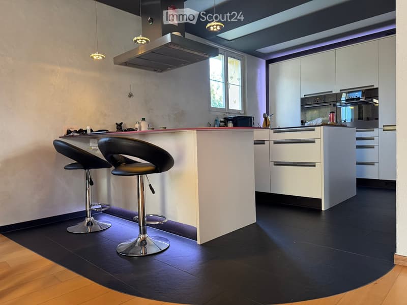 Modern kitchen with white cabinets, black countertops, and a central island with two black stools. Features include an oven, microwave, and a sleek faucet.
