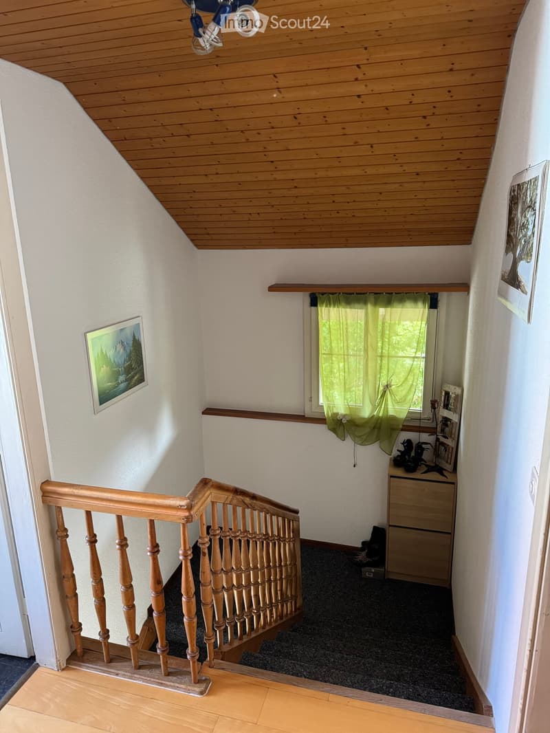 Staircase with wooden railing and steps, leading to a room with a window, green curtains, and a small table with decorative items.