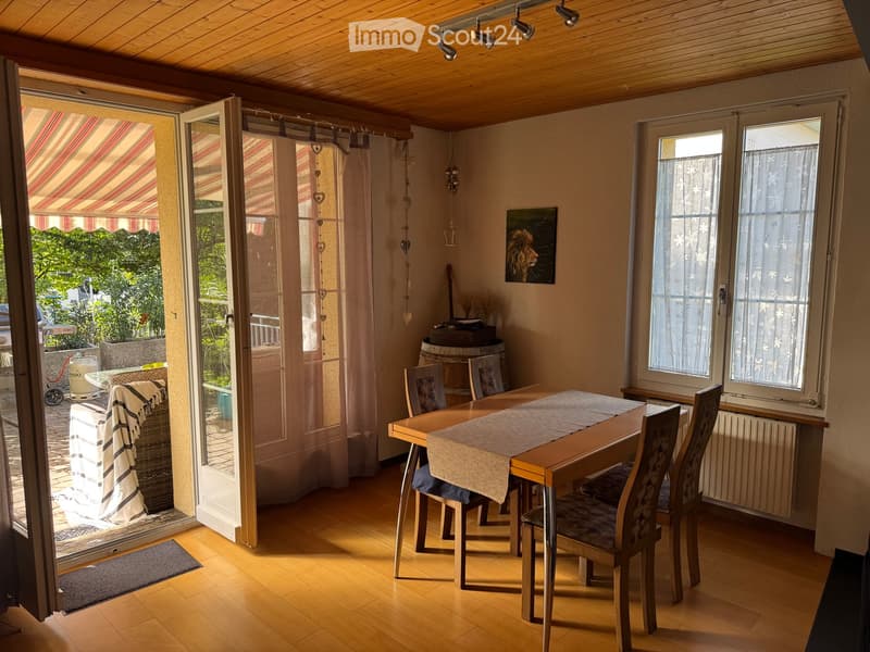 Bright dining room with wooden floor, large windows, dining table with chairs, picture frame on wall, and open sliding doors leading to a patio.