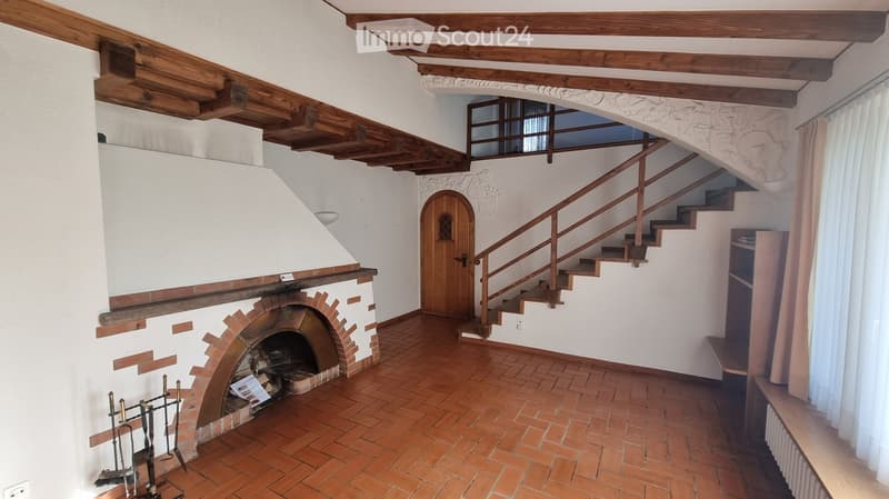 Hallway with exposed wooden beams, brick fireplace, wooden staircase leading to an upper level, and a wooden door.