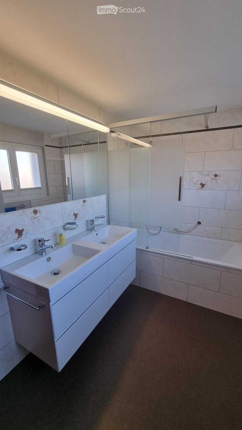 Modern bathroom with a double sink, large mirror, bathtub, and sleek fixtures.
