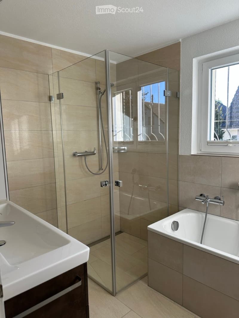 modern bathroom with a glass shower enclosure, white bathtub, and a large window providing natural light