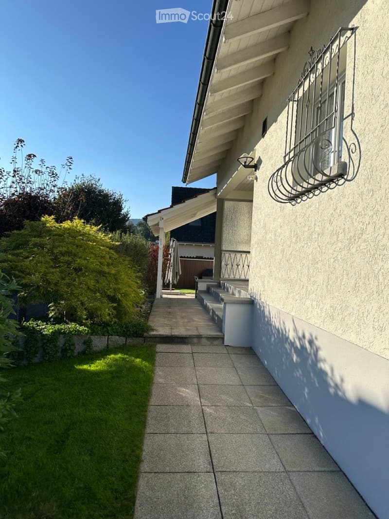 Gray stone walkway, well-maintained green grass, concrete staircase, black railings, outdoor lighting, white exterior walls, gable roof