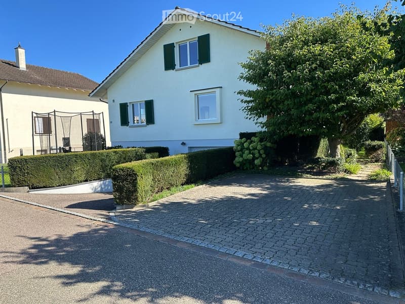 Two-story house, white exterior, green shutters, paved driveway, garden, hedge, tree, fence