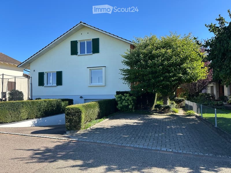 Detached house, white exterior, green window shutters, brick driveway, green hedges, central tree