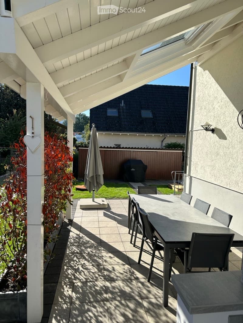 covered patio with table and chairs, large plant with red leaves, patio umbrella, black grill, wooden fence, tiled floor