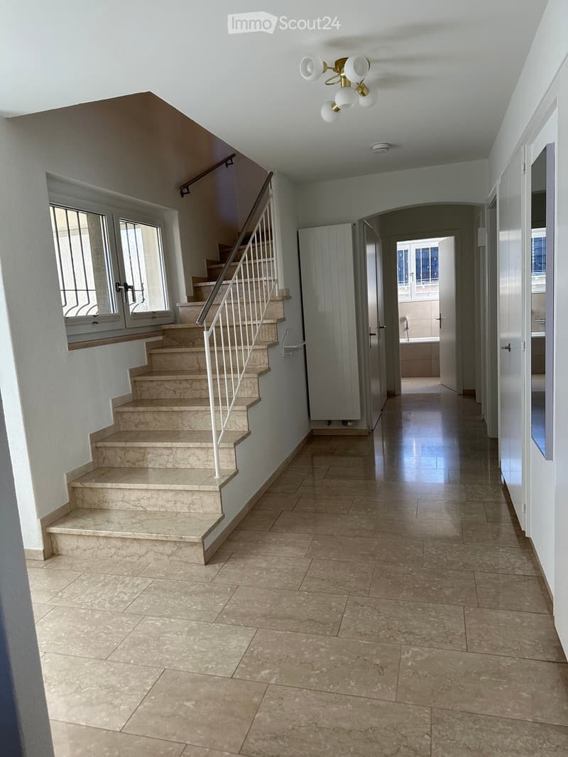 Empty hallway with staircase, tiled floor, and white walls; two doors at the end