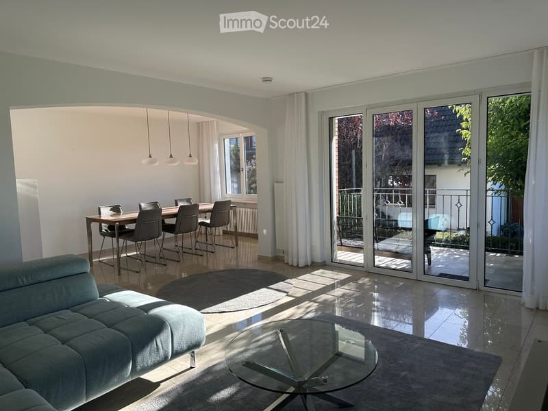 Dining room and living room area, wooden dining table, modern chandeliers, white tiles, blue sofa, glass table, glass sliding doors