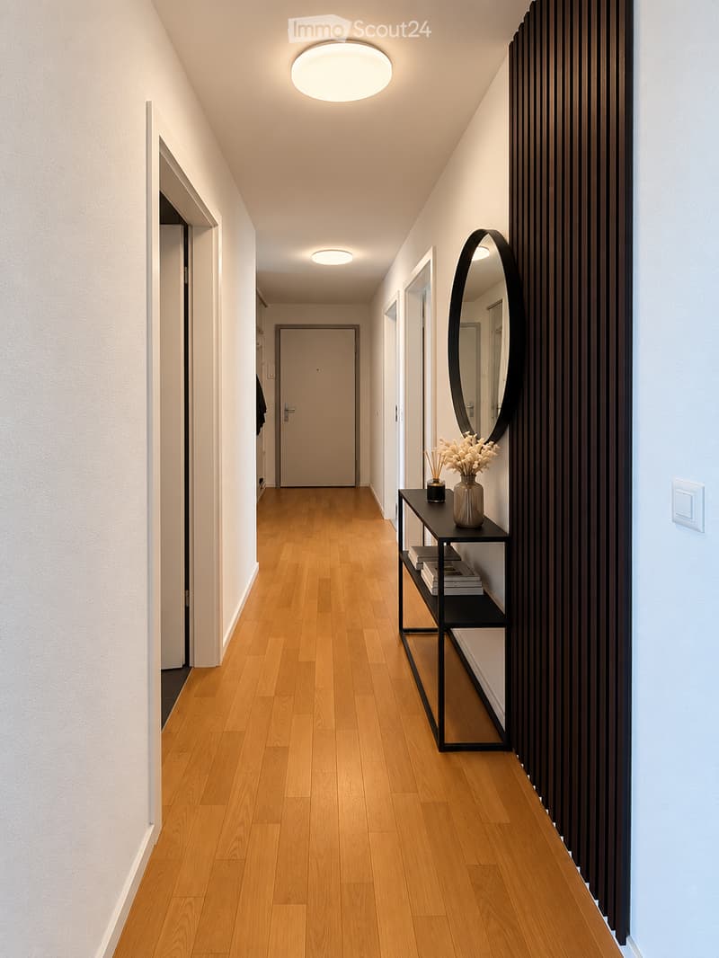 Modern hallway with wooden flooring, white walls, recessed lighting, and a black shelf with a vase and books.