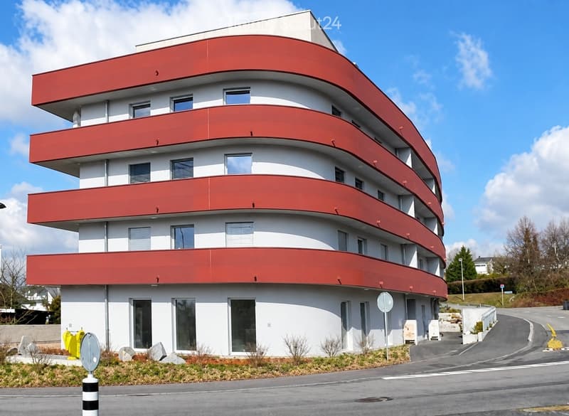 Modern, multi-story building with white walls and red accents, featuring large windows and balconies.