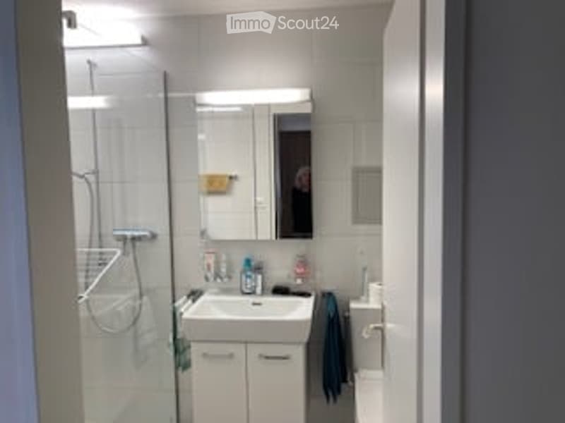 Modern bathroom with white tiles, a sink, mirror, shower, and a towel hanging on the side.