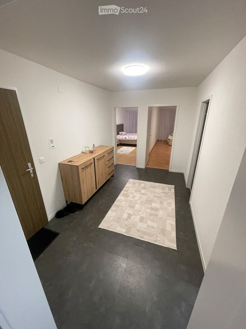 Hallway with dark flooring, white walls, a small wooden cabinet with drawers, and a patterned rug. Two open doors lead to bedrooms.