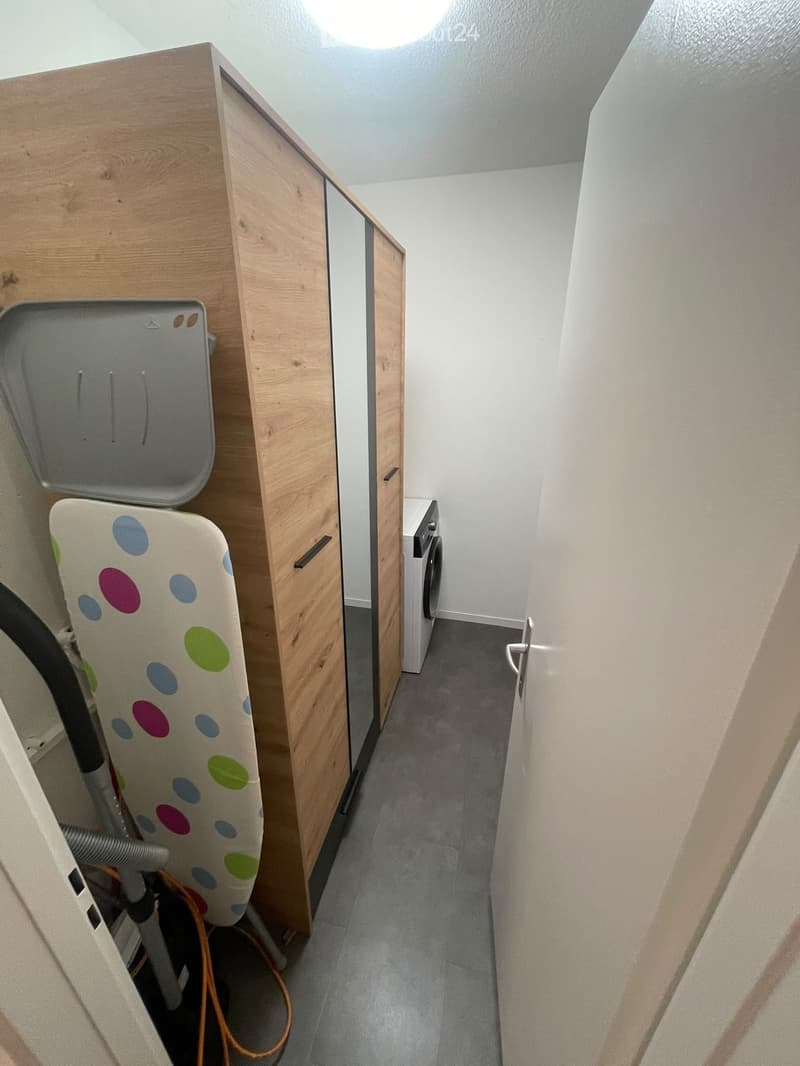 Narrow hallway with wooden cabinets, a washing machine, and a vacuum cleaner with accessories stored on the left side.
