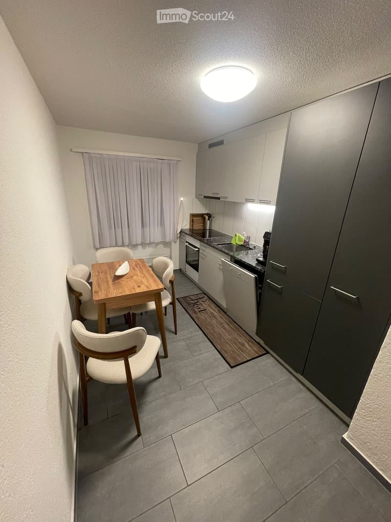 A compact kitchen and dining area with modern grey cabinets, a wooden dining table with four chairs, and a sink with a faucet.