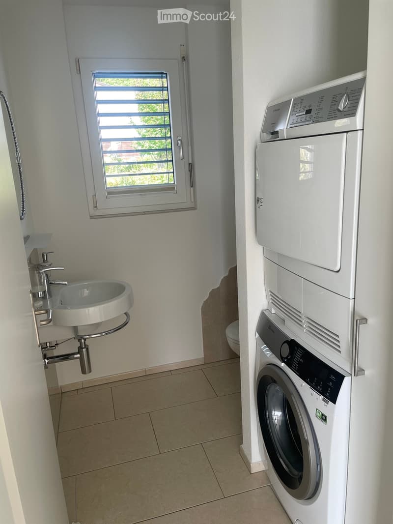 Modern bathroom with a wall-mounted sink, a window, and stacked washing machine and dryer.