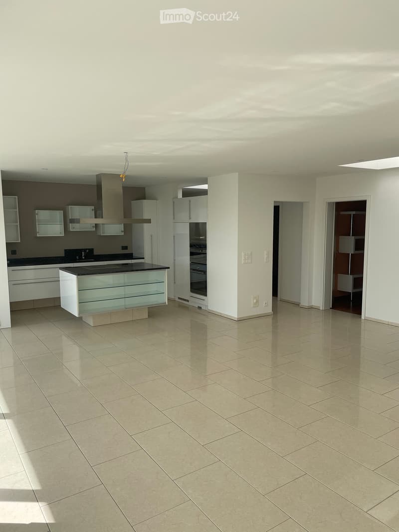 Modern, unfurnished kitchen with white cabinets, stainless steel appliances, and a central island with glass panels.