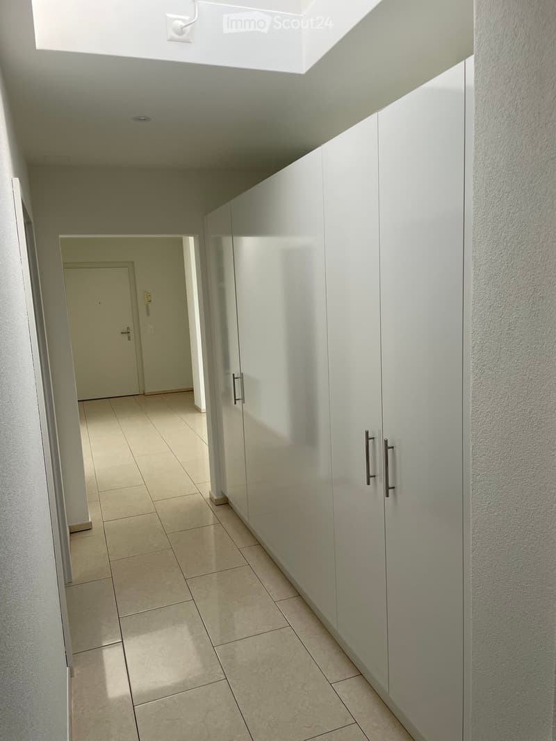 Empty hallway with tiled floor, white walls, built-in cabinets, and a closed door at the end.