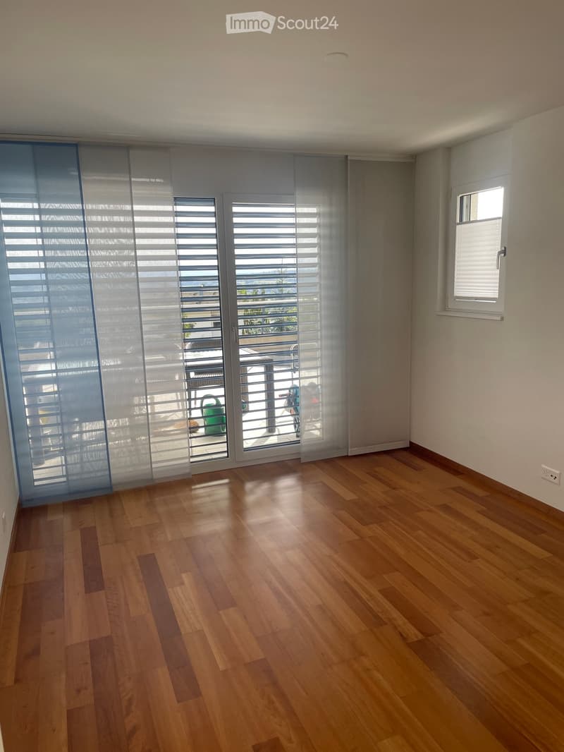 Empty room with wooden flooring, large sliding glass doors with blinds, and a small window on the right side.