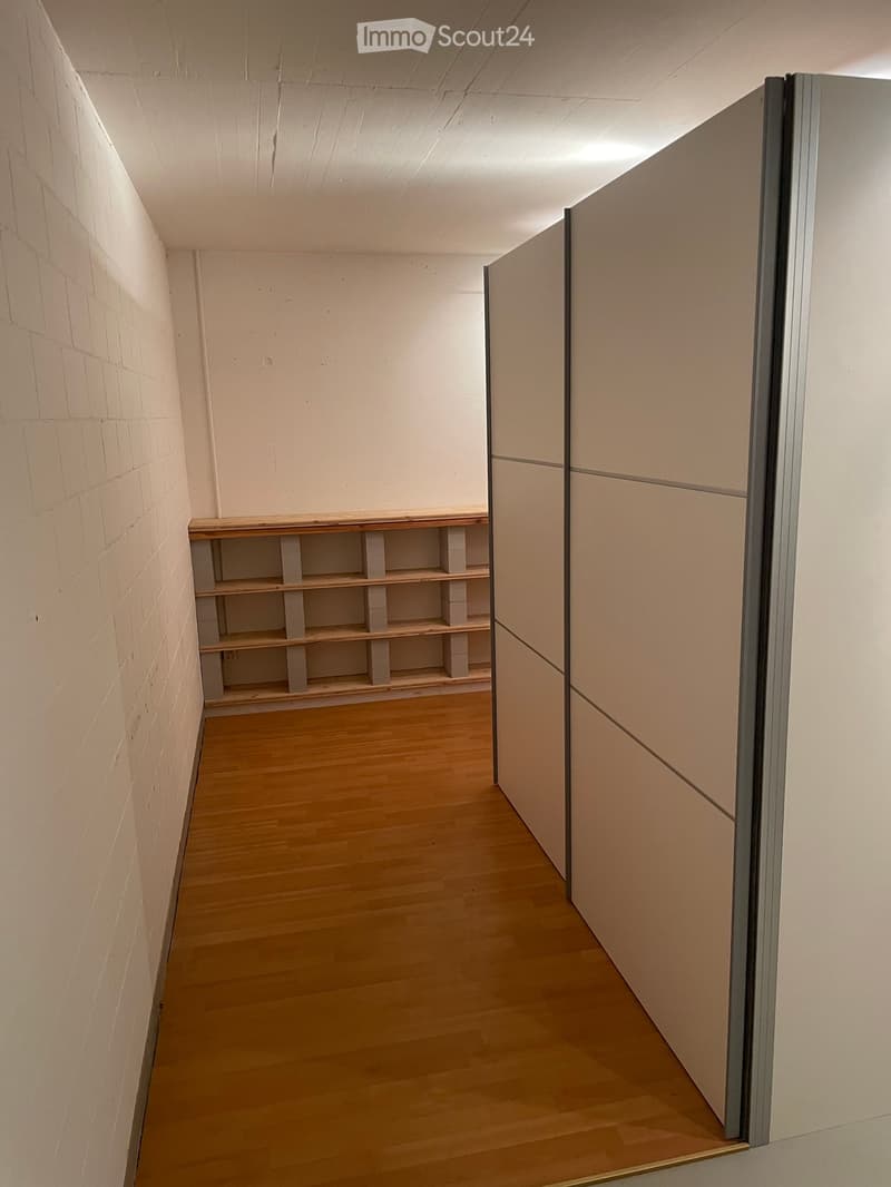 Empty hallway with wooden flooring, white walls, and a built-in wooden shelf unit on one side.