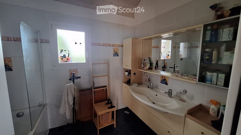 Bathroom with a double sink, mirror cabinet, towel on a rack, small wooden stool, and a shower area with a window.